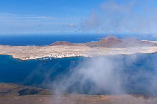 View of La Graciosa Island in the Canary Islands and the main town of Caleto Del Sebo with with clouds forming in the channel between Lanzarote and La Graciosa.