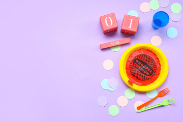 Table setting with whoopee cushion, confetti and calendar for April Fools Day on lilac background