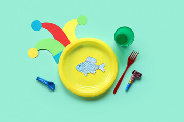 Table setting with paper fish and party decor for April Fools Day on turquoise background