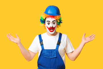 Surprised young man as clown in jumpsuit and helmet on yellow background