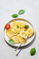 Ravioli pasta with parmesan, tomatoes and basil in a plate on a light  background with shadow.