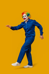 Funny young man as clown in coverall on yellow background