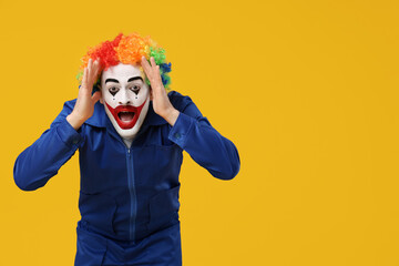 Surprised young man as clown in coverall on yellow background