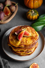 Stack of pumpkin and pancakes with honey and figs on a dark background with fresh fruits and vegetables.