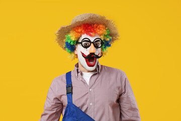 Surprised young man as clown farmer on yellow background