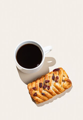 Coffee espresso cup and fresh maple pecan bun pastry on a beige  background with shadow.