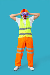 Shocked young man as clown builder on blue background