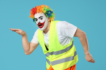 Surprised young man as clown builder dancing on blue background