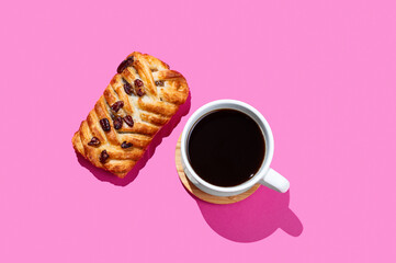 Coffee espresso cup and fresh maple pecan bun pastry on a pink background with shadow.