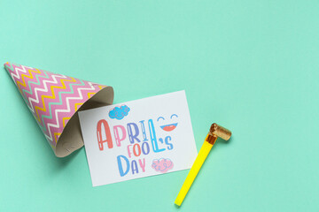 Fototapeta premium April Fool's Day greeting card with party hat and toy blower on pastel turquoise background, festive holiday flat lay with copy space