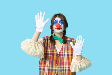 Young woman dressed as sad clown on blue background. April Fool's day celebration