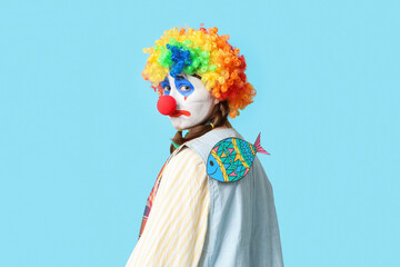 Young woman dressed as sad clown with paper fish attached to her back on blue background. April...