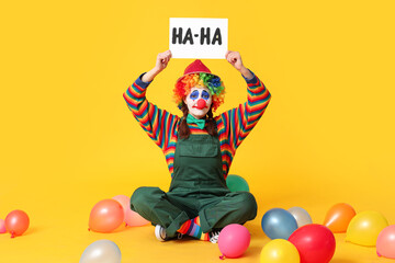 Young woman dressed as sad clown holding balloons and card with text HA-HA on yellow background. April Fool's day celebration