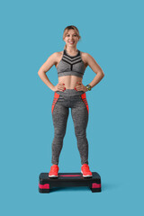 Young female fitness trainer standing on aerobic stepper against blue background