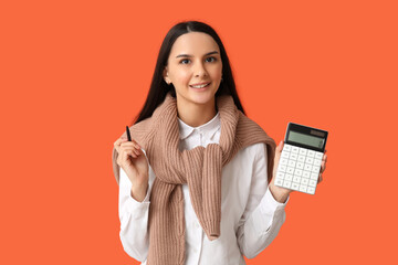 Beautiful young woman with calculator and pen on orange background