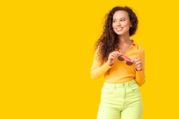 Beautiful African-American woman with sunglasses on yellow background