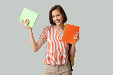 Beautiful female student with notebooks on grey background