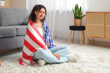 Beautiful young happy African-American woman with USA flag sitting on floor at home