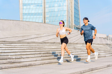 Couple jogging on urban steps with modern buildings in the background during a sunny day