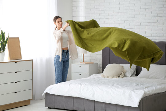 Young woman putting green blanket on bed at home