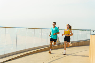Couple enjoys morning run along seaside boardwalk on a sunny day, promoting fitness and wellness