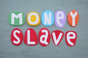 Money slave, modern social slavery, creative text composed with hand painted multi colored stone letters over green sand