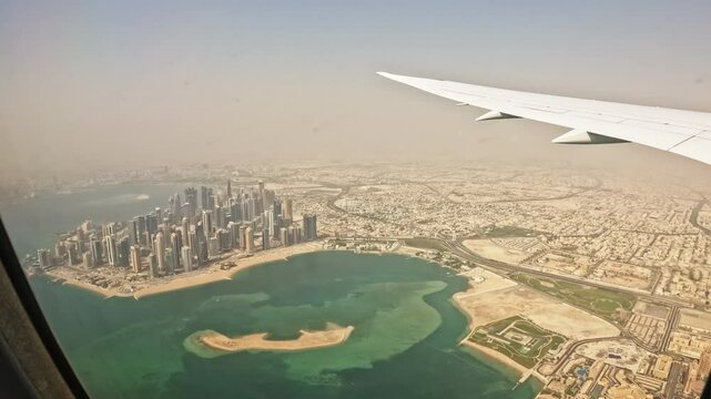 Airplane wing flying over desert area with capital city on coastline