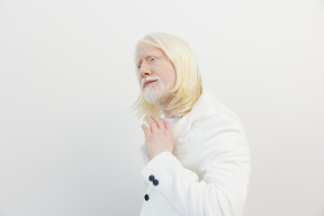 Portrait of a thoughtful man with long white hair and a beard, wearing a white coat against a...