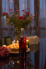 Bottle of red wine, cake with candles, bouquet of flowers and fruits. Warm romantic scene. Festive table decor