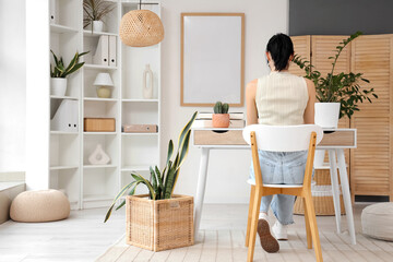 Young woman working at desk in light home office, back view