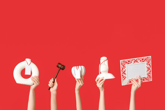 Female hands with auction gavel and antique items on red background