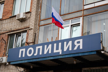 A Russian flag fluttering in the wind and a sign with the inscription "Police" in Russian. The entrance to the police station building