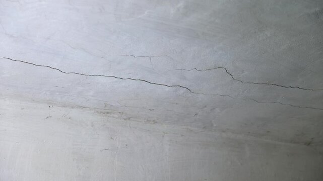 Close up. Old white abandoned cement ceiling with cracks and cobwebs. Dirt and dust all around, indicating possible age or structural stress.