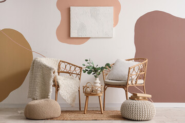 Armchairs, coffee table with branches in vase and poufs near colorful wall in room