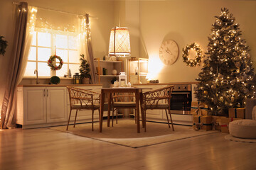Interior of dark kitchen with glowing Christmas tree, dining table and counters at night