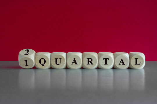 Turned a cube and changes the German expression '1 Quartal' (first Quarter) to '2 Quartal' (second quarter). Beautiful red background, grey table. Business concept.