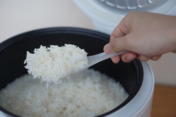 Hands use a plastic spoon to scoop rice from the electric rice cooker. Concept, cooking, checking...