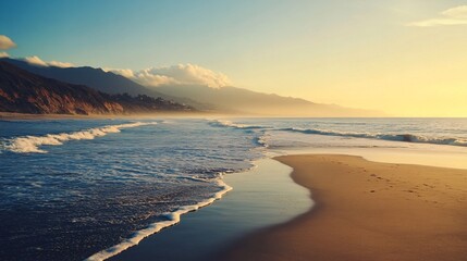 Ocean waves gently rolling into sandy beach at sunset with mountains in background