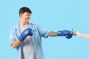 Young man in boxing gloves and blue ribbon on color background. Prostate cancer awareness concept