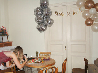 bride-to-be in a red dress making a photo of a table with snacks at a hen party in a room decorated with balloons 