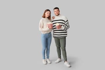 Happy young couple with buckets of popcorn on grey background