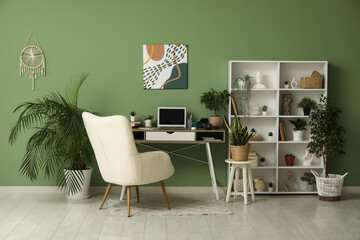Stylish workplace with laptop, shelving unit and different houseplants near green wall at home