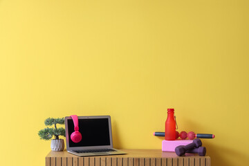 Laptop with headphones and sports equipment on commode near yellow wall