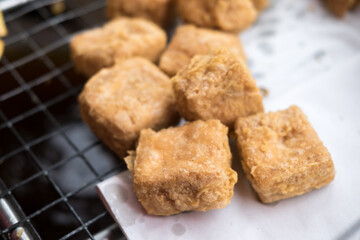 Golden-brown, slightly porous cubes of fried tofu sit on white absorbent paper over a black wire rack. Simple and freshly cooked.