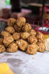 Pile of golden-brown, crispy bala-bala (vegetable fritters) or bakwan sayur spills from a metal basket onto white paper. Savory Indonesian snack.