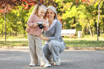 Fototapeta premium Cute little girl with photo camera and her mother in park on autumn day
