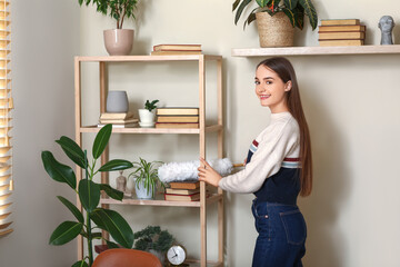 Young woman cleaning dust on book shelves in living room