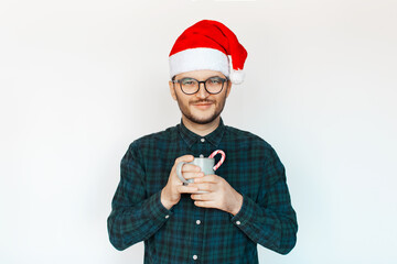 Portrait of young man in Santa hat with cup of hot cacao with candy cane in hand, white background.