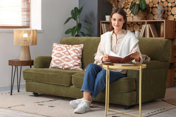 Beautiful young woman reading book on coffee table while sitting on sofa in living room