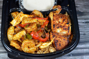Mixed seafood of fish fillet, shrimps and squid grilled or cooked in oven with slices of tomatoes, onions, green peppers and red sauce, served on top of red fish rice and Tahini salad, seafood meal